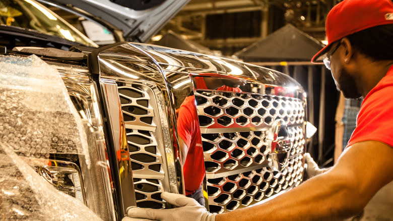 A worker adjusts the grille of a Nissan Titan in a factory.
