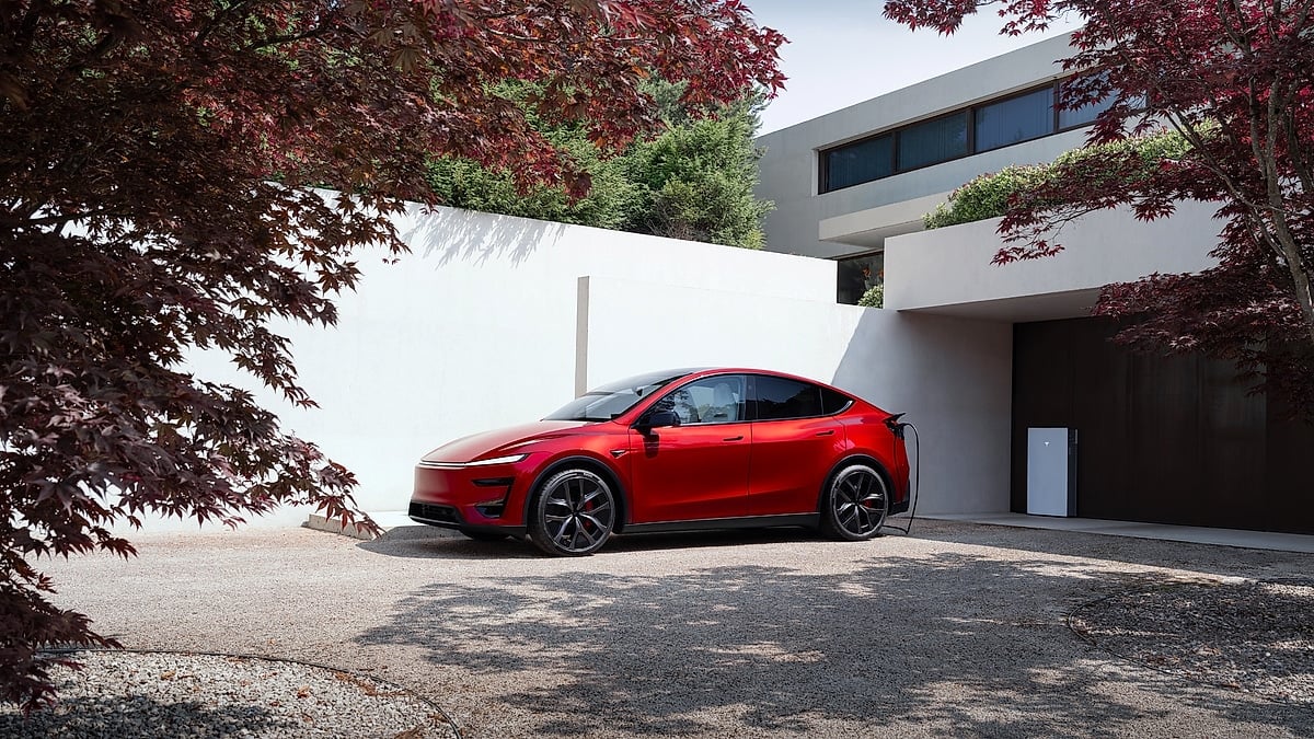 Red Tesla Model Y Performance parked and charging beside a modern home with a Tesla Wall Connector.
