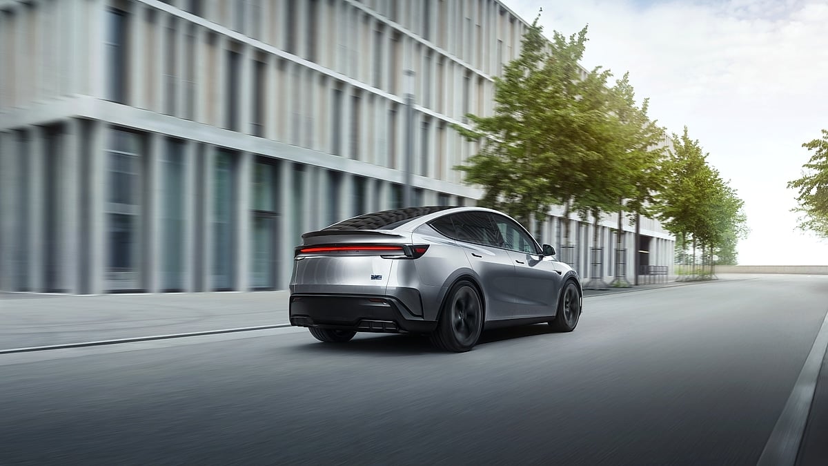 Silver Tesla Model Y Performance driving through a modern urban street, shown from the rear three-quarter angle.