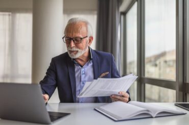Person holding documents, while looking at laptop.