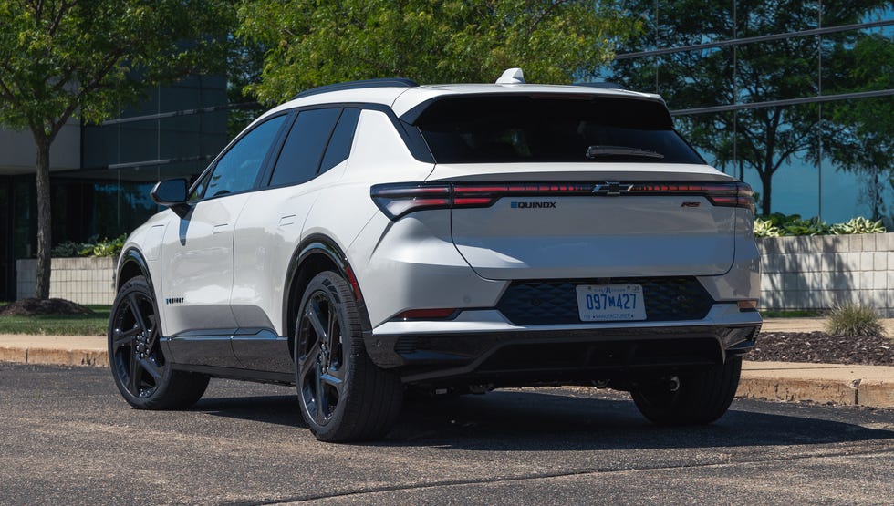 rear three quarter view of a white suv parked in front of a modern glass building surrounded by trees.