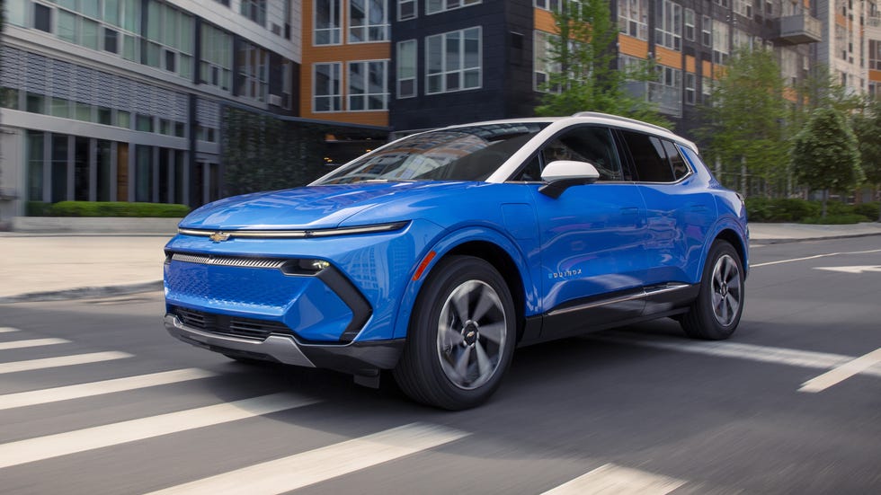 front three quarter view blue suv driving through city street with modern apartment buildings in background.