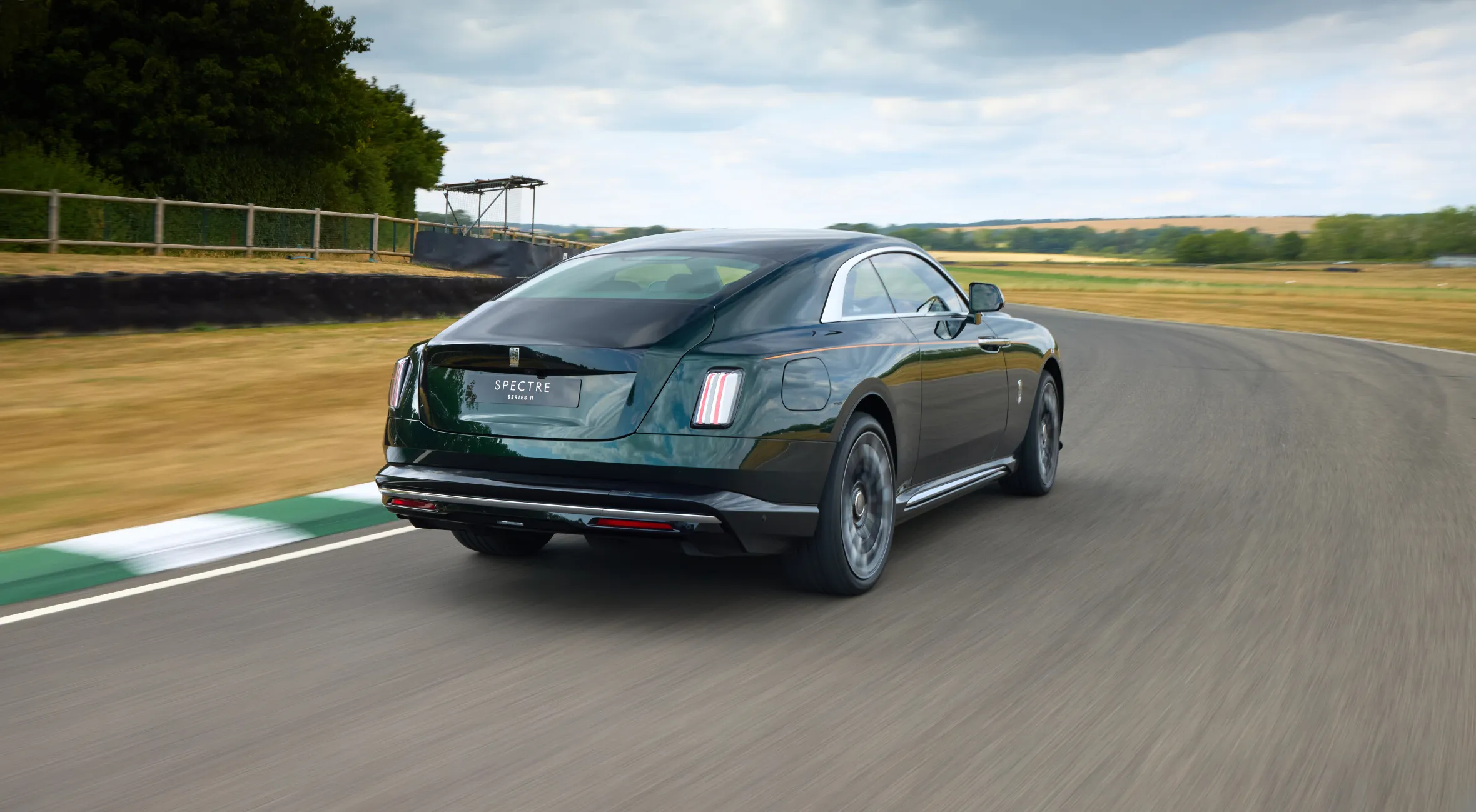 Rear view of a dark green Rolls-Royce Spectre Series II driving on a racetrack.