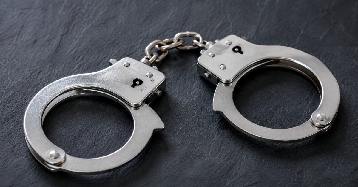 Silver metal handcuffs lie on a dark gray slate surface.