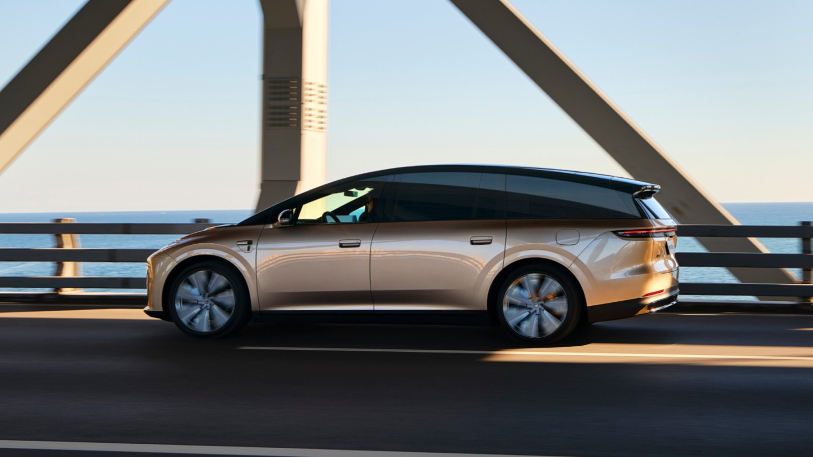 Gold Li i9 electric SUV driving across a bridge, viewed from the side with the sea in the background.